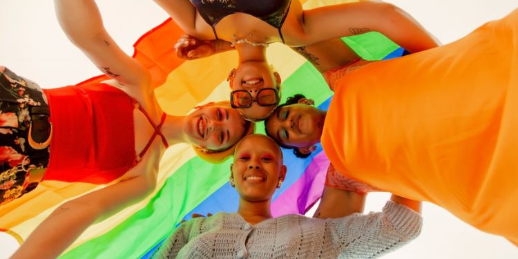 Pessoas LGBTQIAPN+ sorrindo sob bandeira colorida em sinal de união e orgulho.