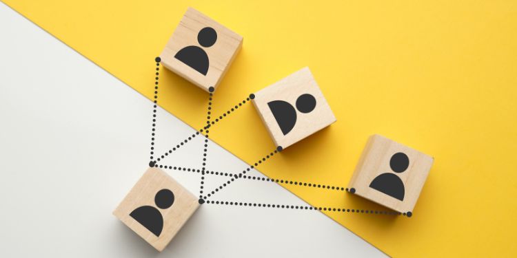 Quatro blocos de madeira com ícones de pessoas conectados por linhas pontilhadas, representando rede de conexões ou estrutura organizacional.