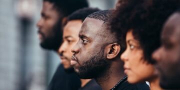 Grupo de pessoas negras olhando na mesma direção em um ambiente externo.